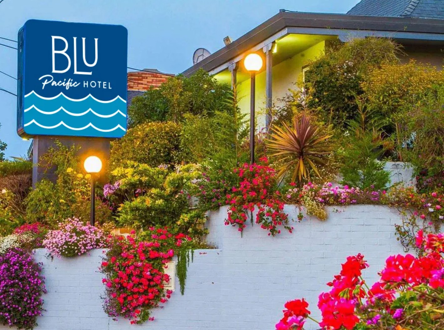 Hotel sign reads 'BLU Pacific Hotel' with a blue background and wave design, surrounded by colorful flowers and greenery.