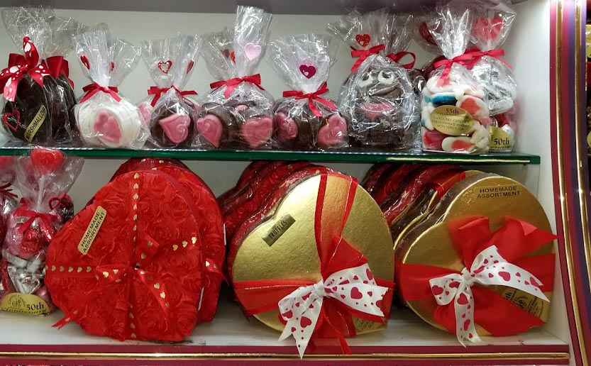 Display of heart-shaped chocolates and gift boxes with ribbons on glass shelves.