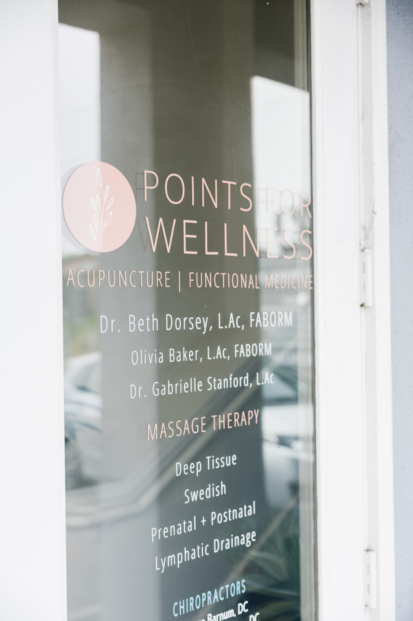 Glass door with wellness and healthcare service information, including names of practitioners and treatments offered.