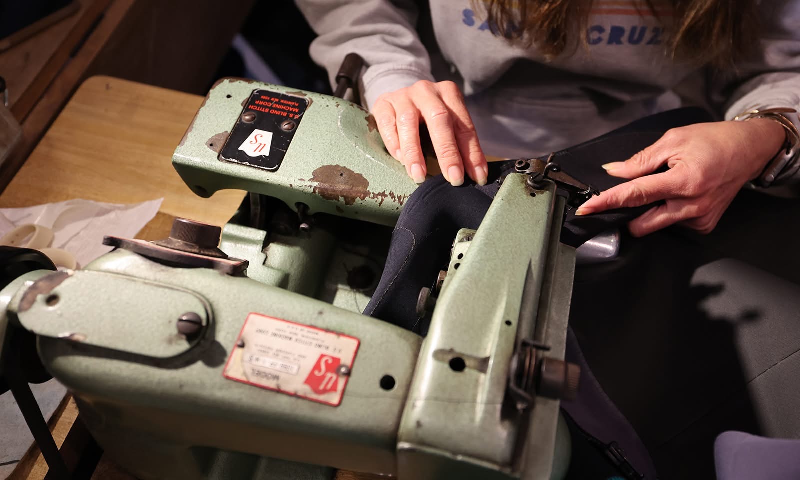 Person using a green industrial machine on a wooden surface, with hands adjusting or operating it.