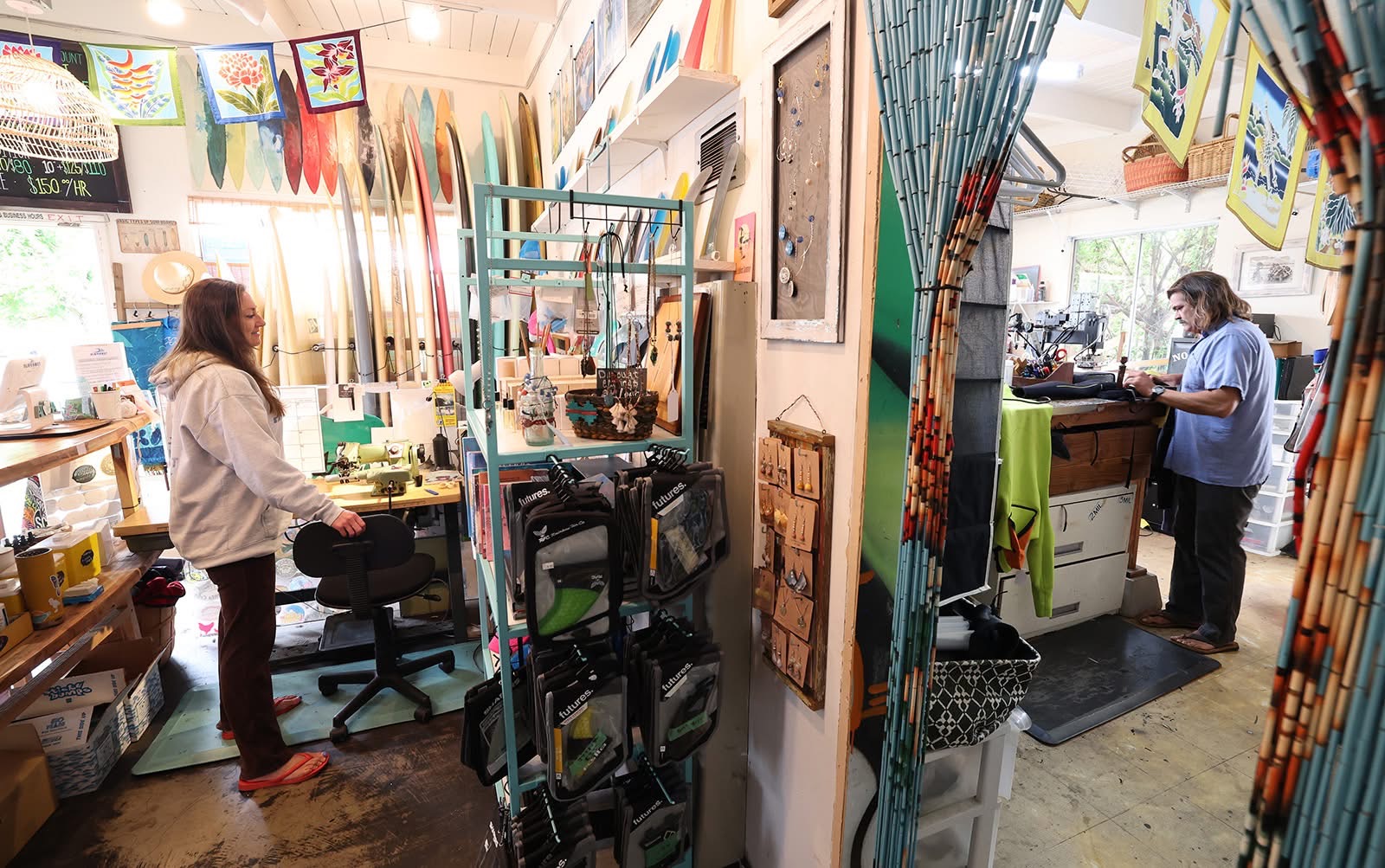 Two women in an art studio with colorful paintings, supplies, and decorations, working at separate stations. Bright, creative environment.