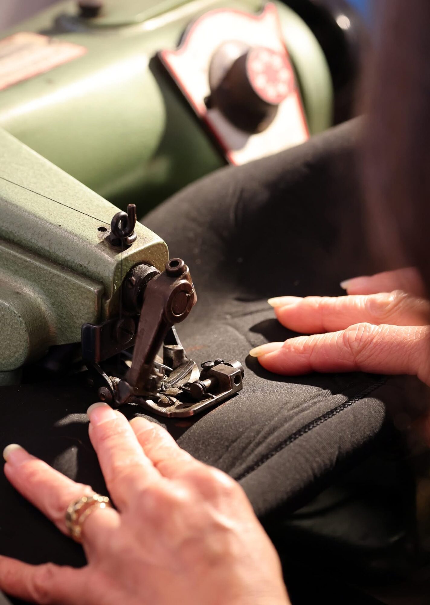 Close-up of hands operating a sewing machine, with fabric and a person's lap visible.