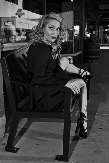 Woman sitting on a bench outside, looking at the camera, with a city background, in black and white.