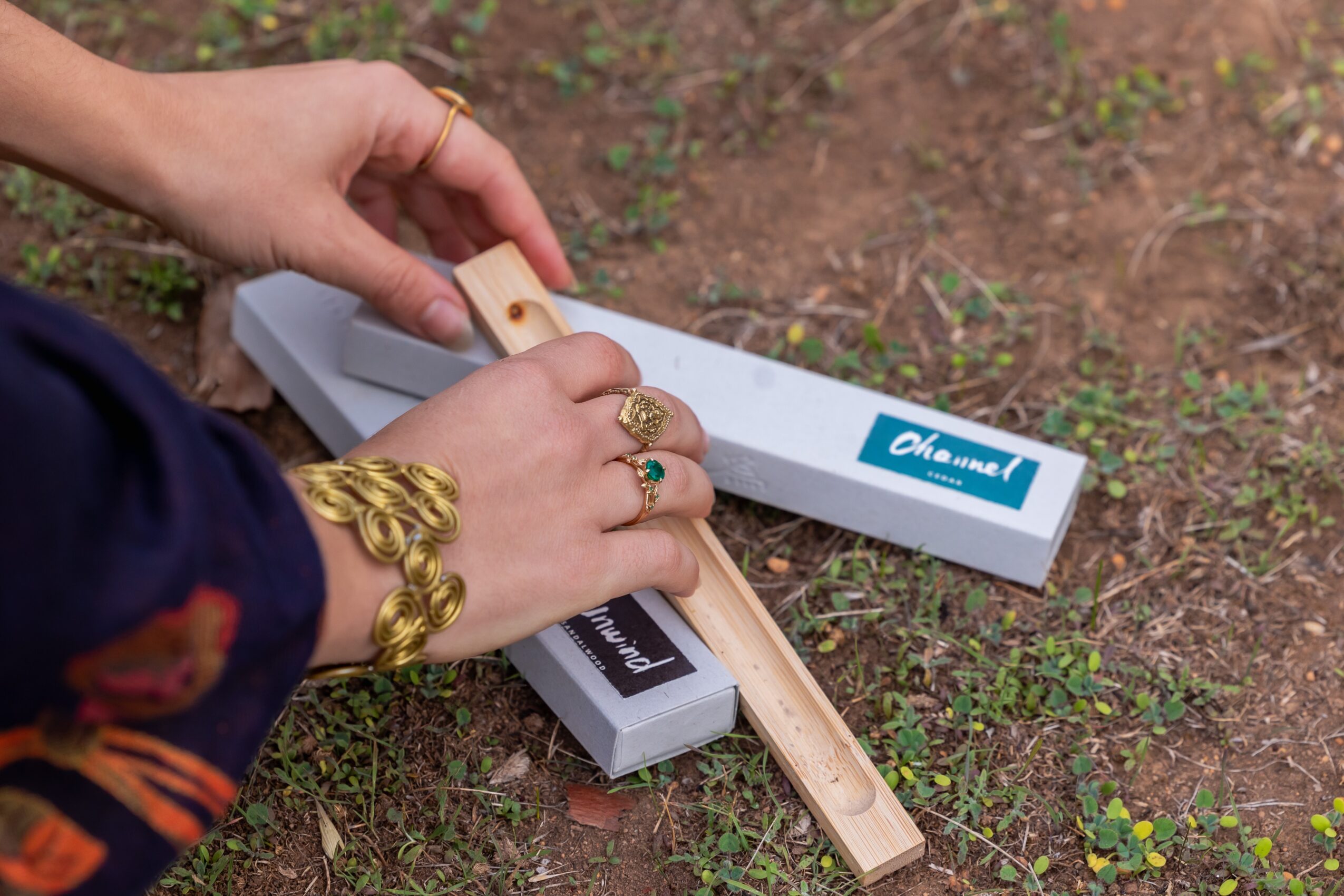 Person's hands using a wooden ruler on a white box outdoors, with grass and soil visible.