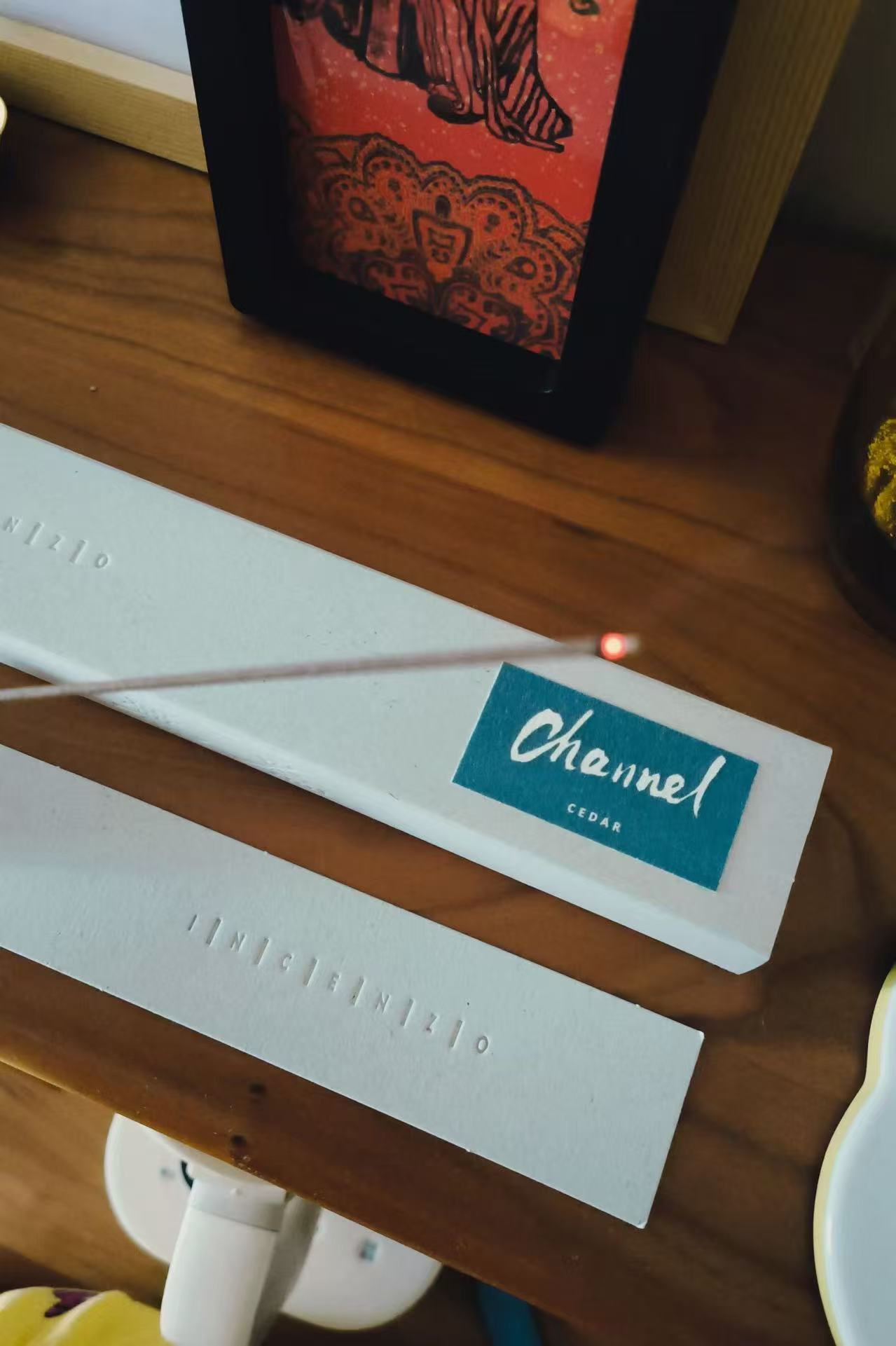 A white bookmark with blue text reading 'Channel' rests on a wooden surface, with a framed artwork in the background.