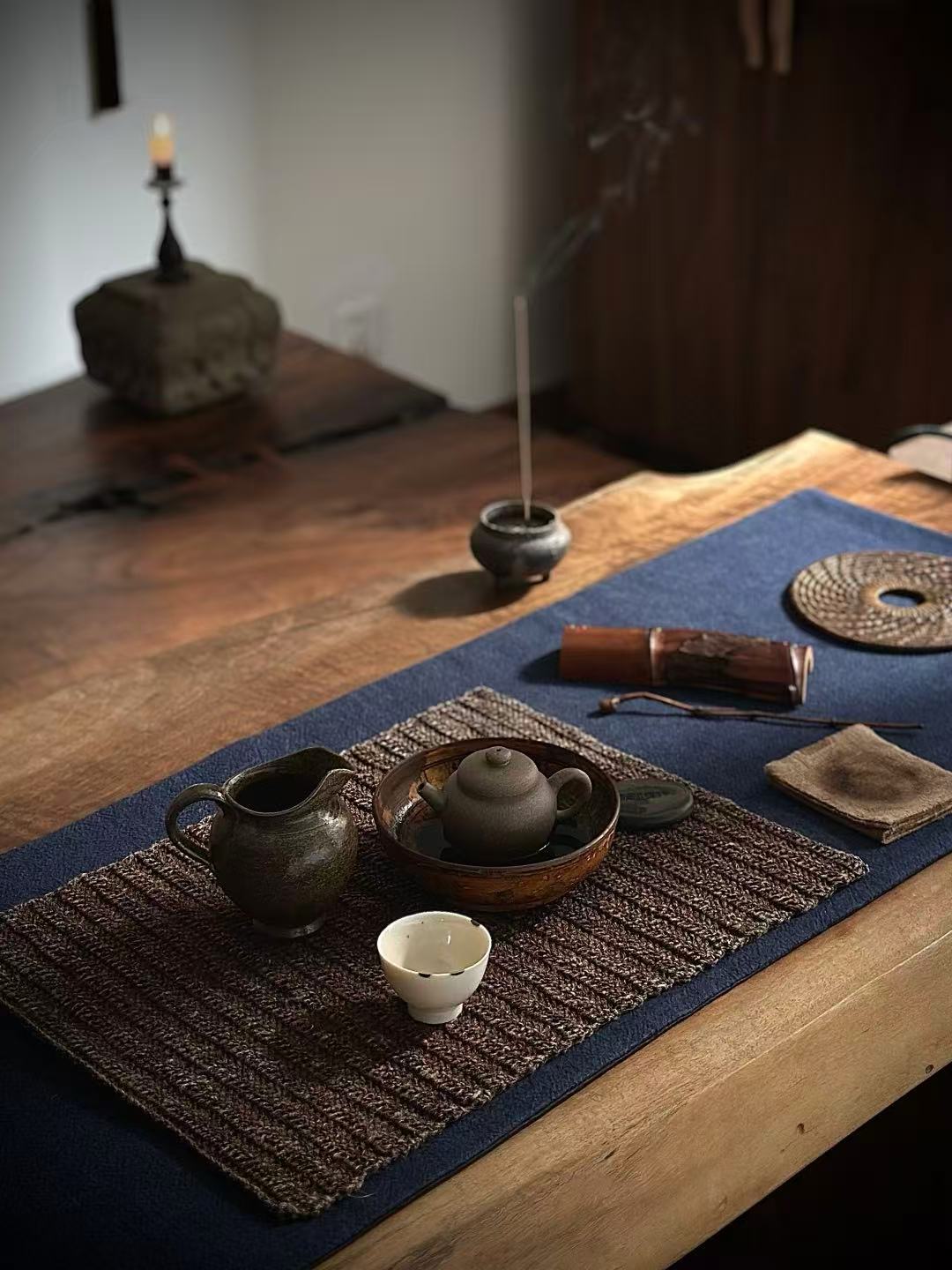 Tea set with teapot, cups, and incense on a table with a blue cloth, in a dimly lit room.