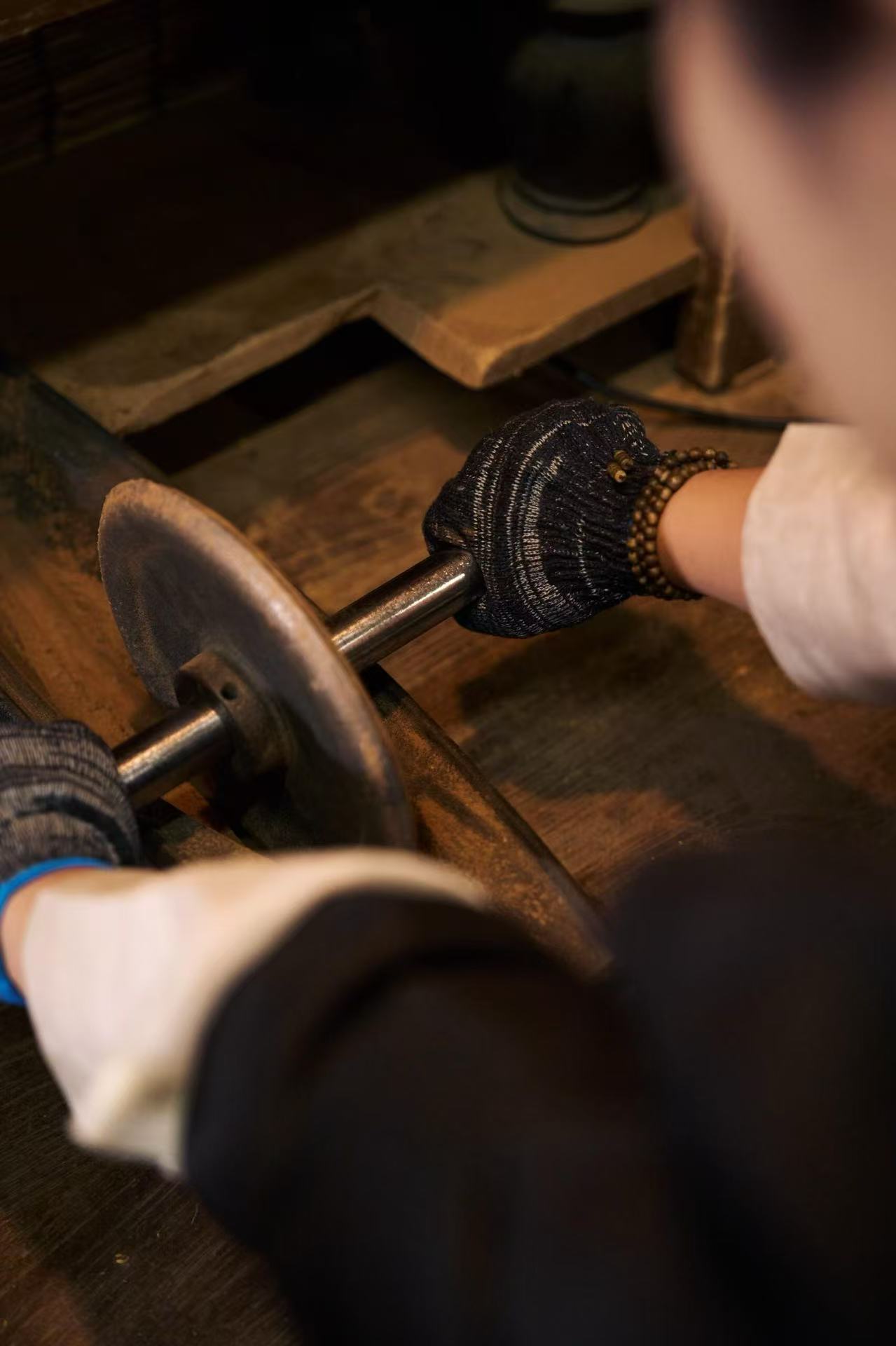 Person wearing gloves working with a metal object on a wooden surface, possibly in a workshop.