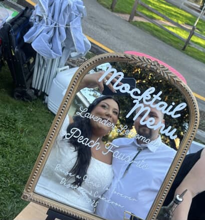 Mirror reflecting a woman in a white dress and a man in a white shirt, with a sign reading 'MacStait Menu' and other text.