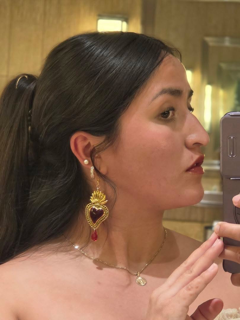Side profile of a woman with dark hair, wearing earrings and a necklace, taking a selfie in a mirror.