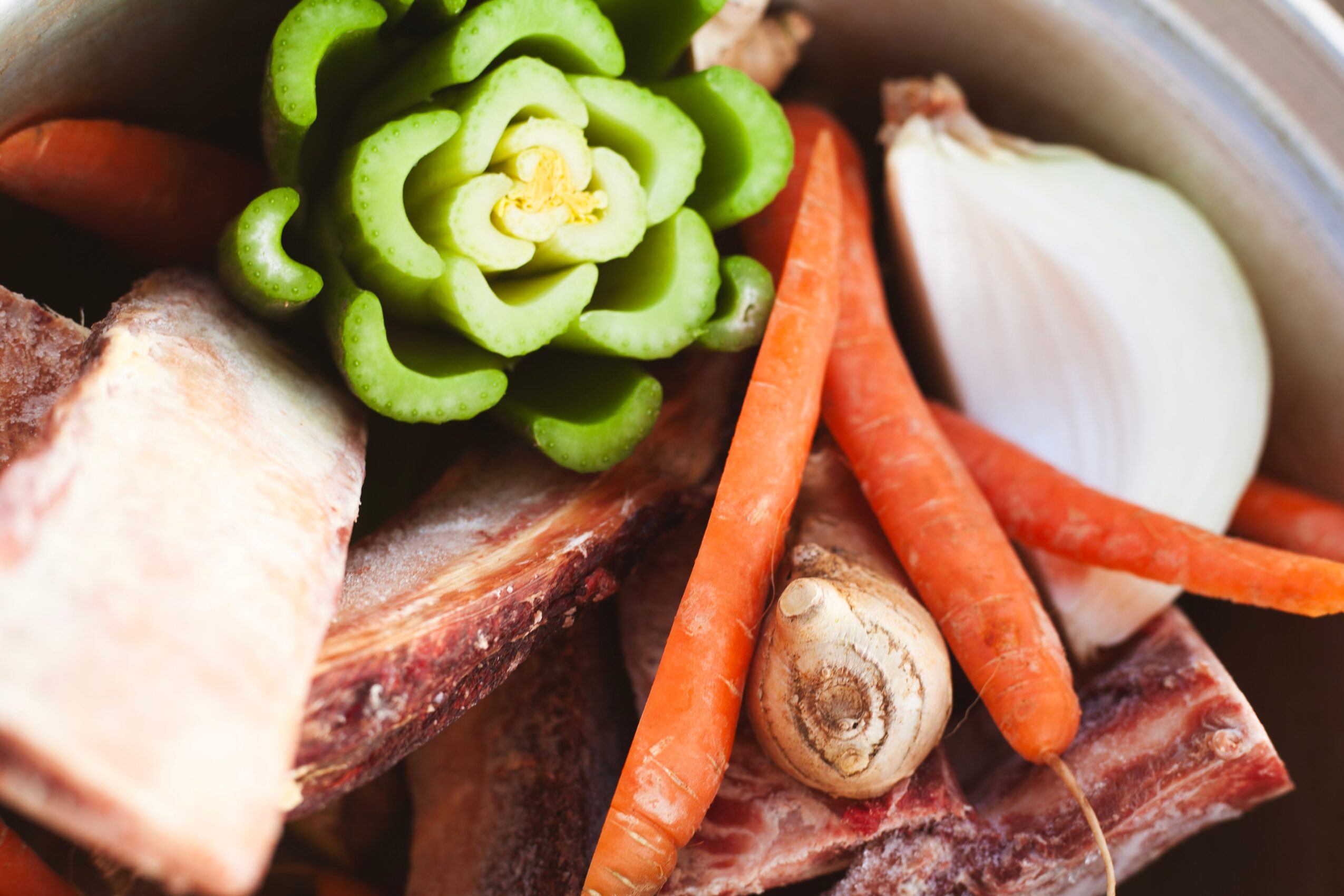 Close-up of fresh vegetables including sliced green bell pepper, carrots, onion, and ginger in a bowl.