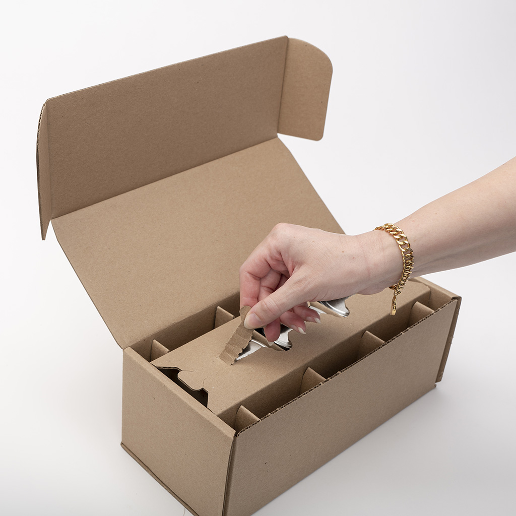 Hand reaching into a cardboard box with compartments, open lid, on a white surface.