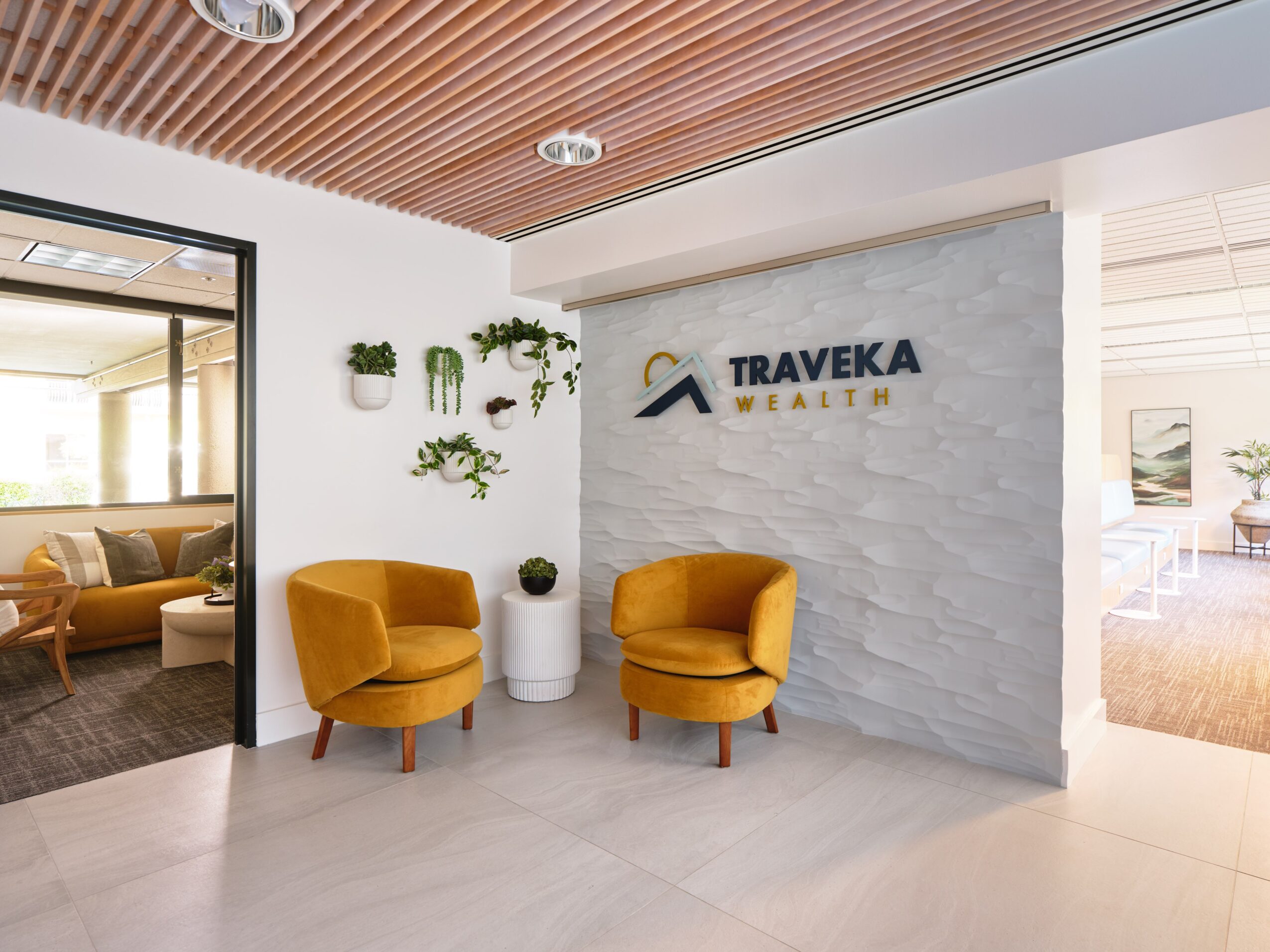 Lobby area with two yellow armchairs, white wall with plants, and a sign reading 'TRAVEKA WEALTH'.