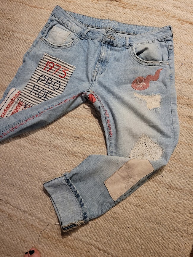 Light blue distressed jeans with patches, lying on a beige textured surface.