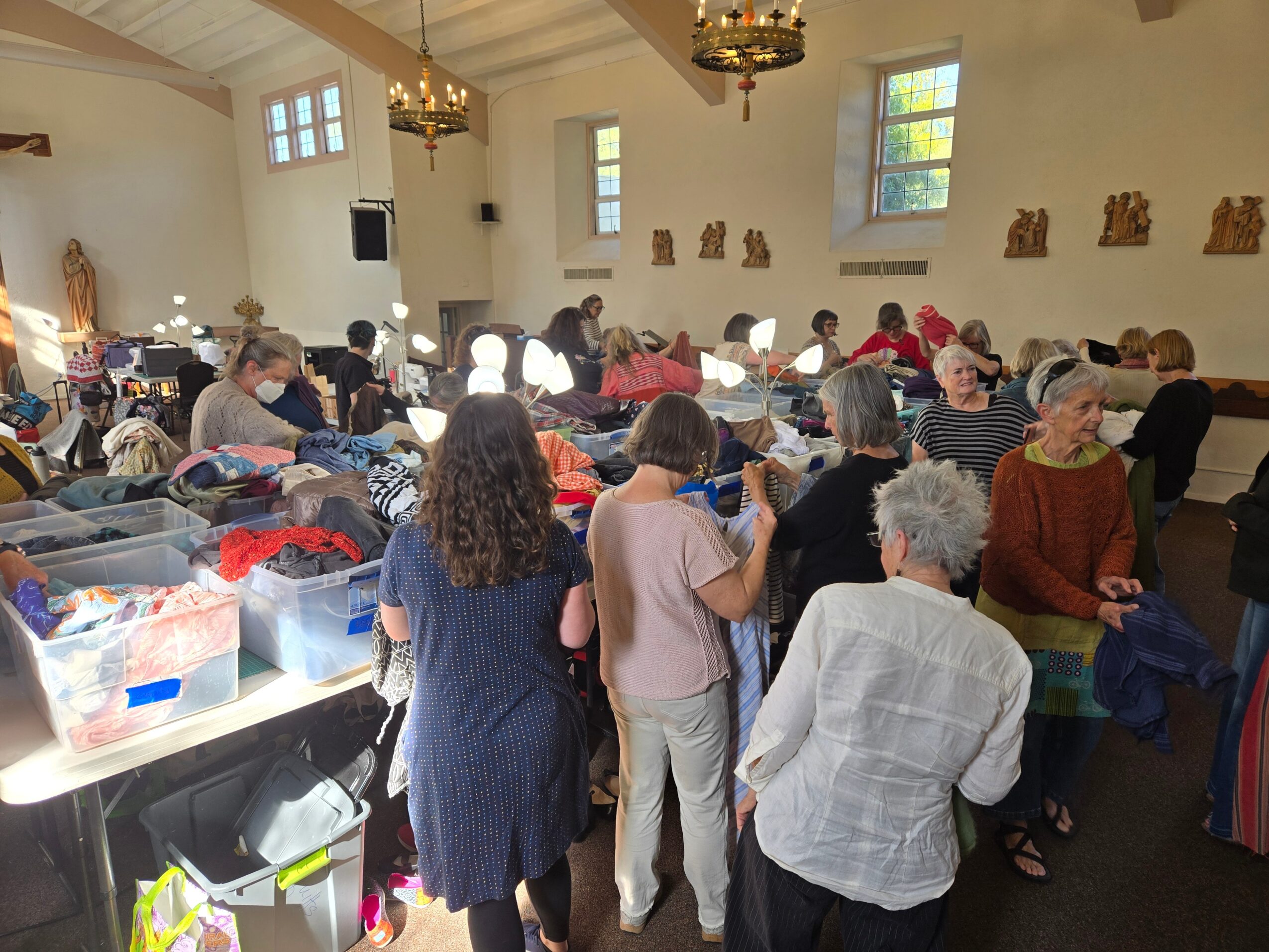 People gathered inside a church with high ceilings, windows, and wooden decorations, engaging in an activity around tables.
