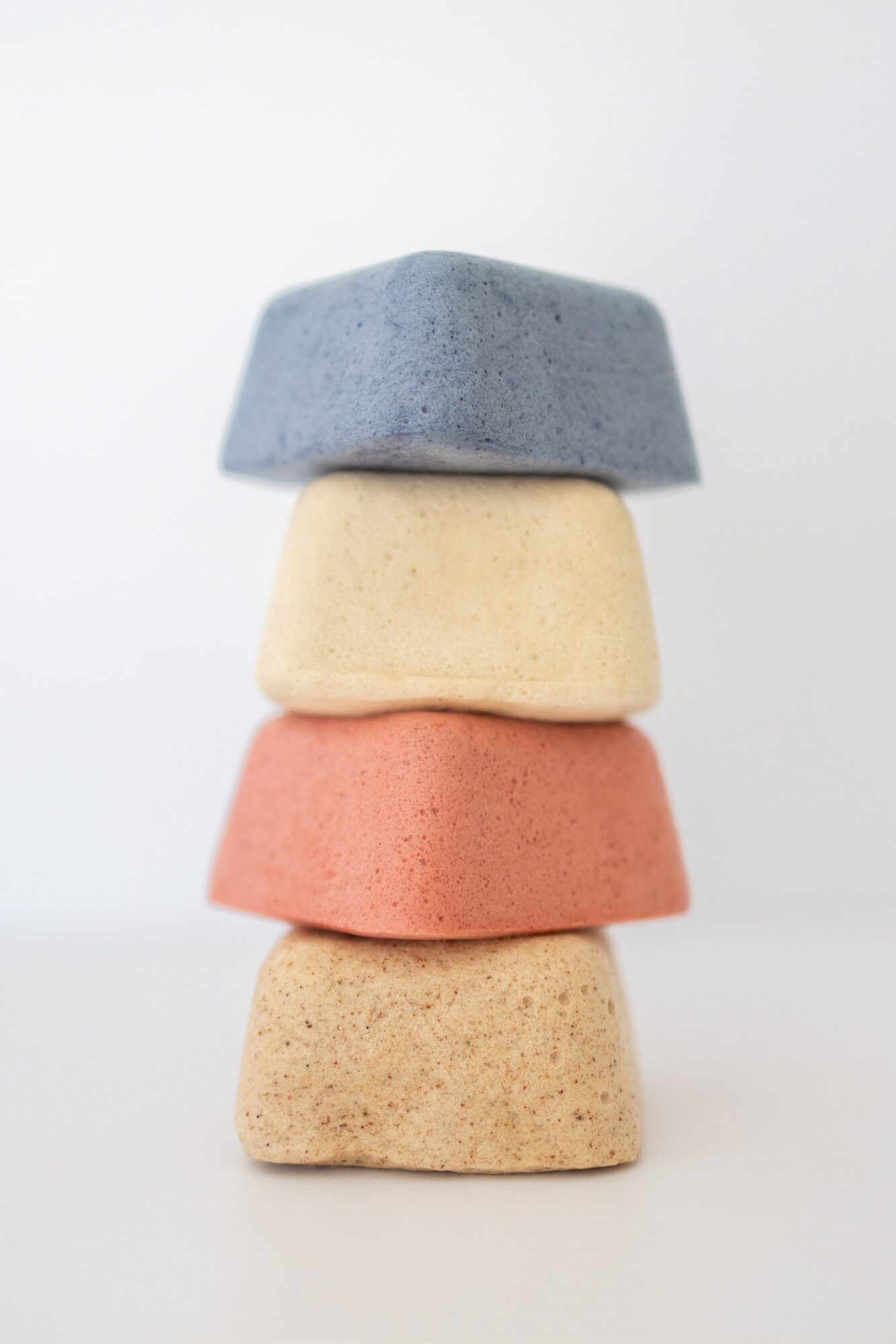 Four stacked sponges in blue, cream, pink, and beige colors against a white background.