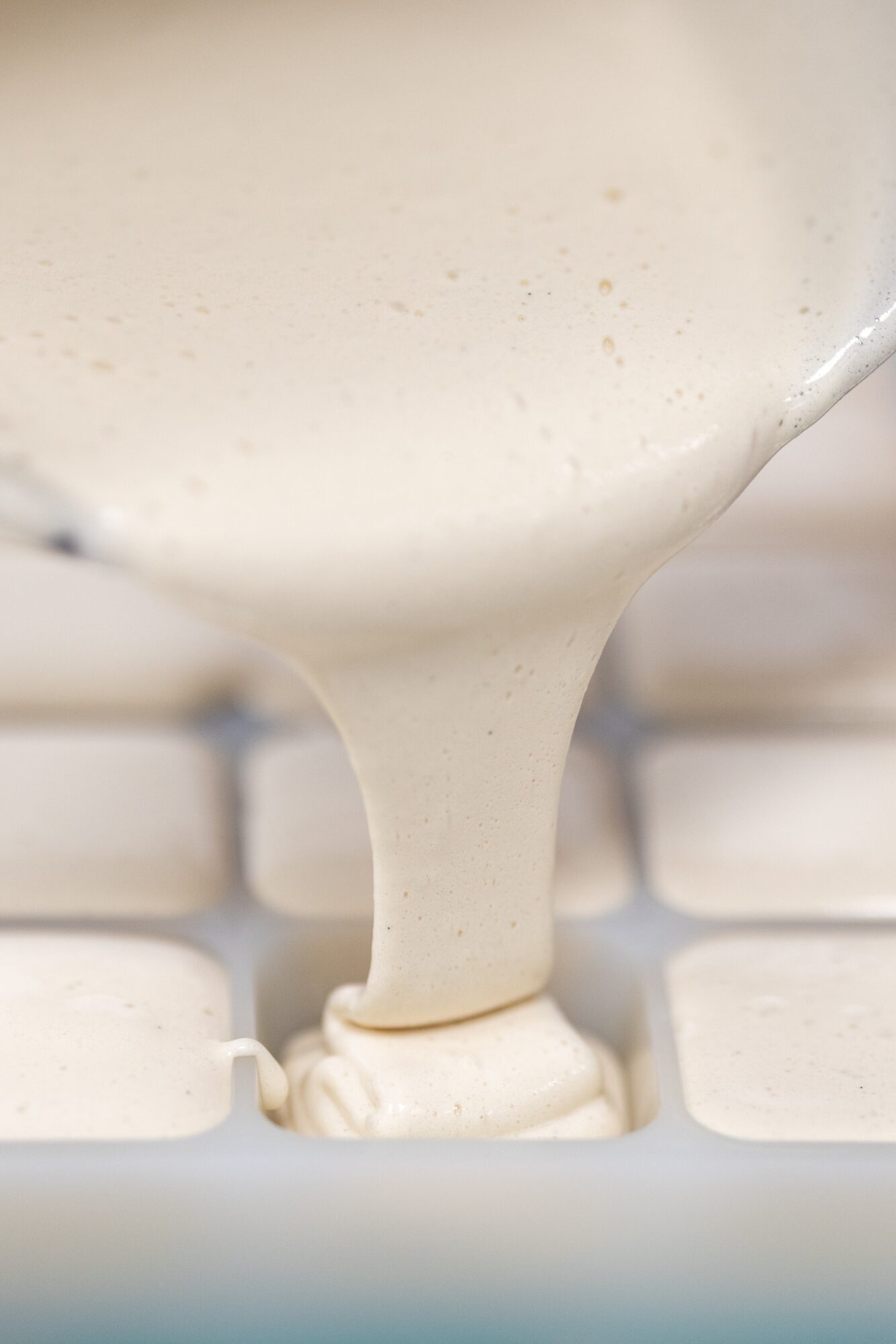 Pouring creamy white sauce onto a white tiled surface, close-up view.
