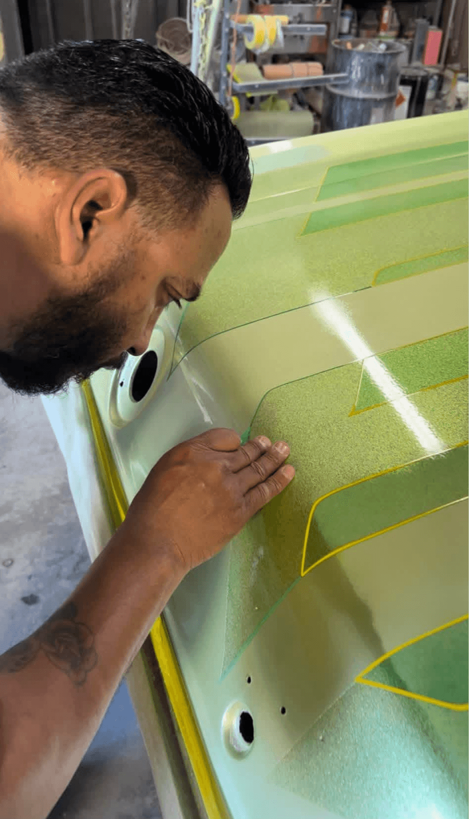 Man working on a green and yellow surface with tools, in a workshop or garage setting.