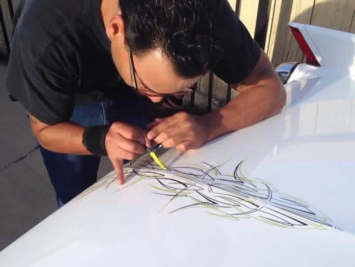 Person drawing on a white surface with a yellow marker, focusing on detailed lines, wearing glasses and a black shirt.