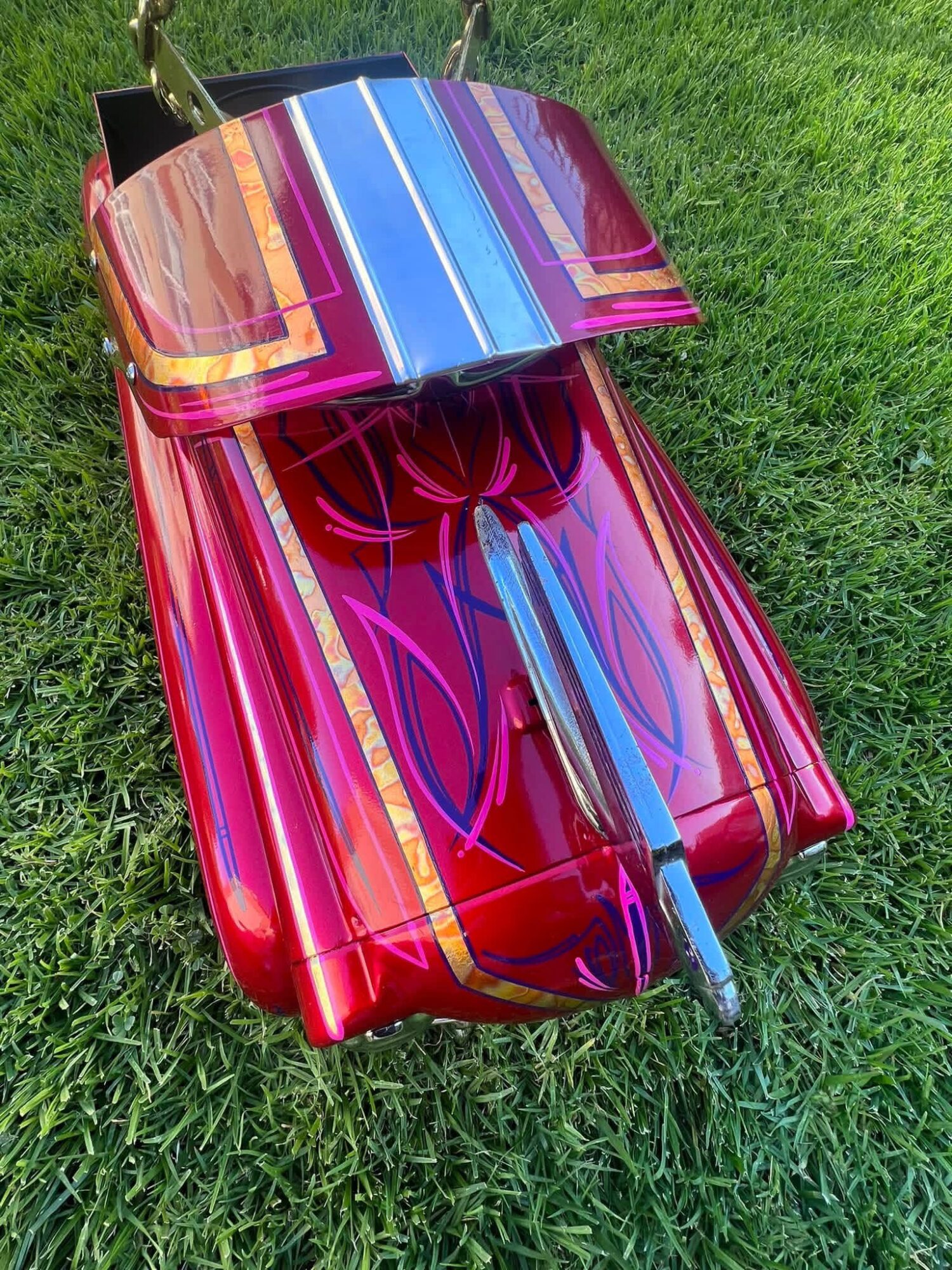 Colorful, shiny toy car with a blue and purple striped roof, on green grass.