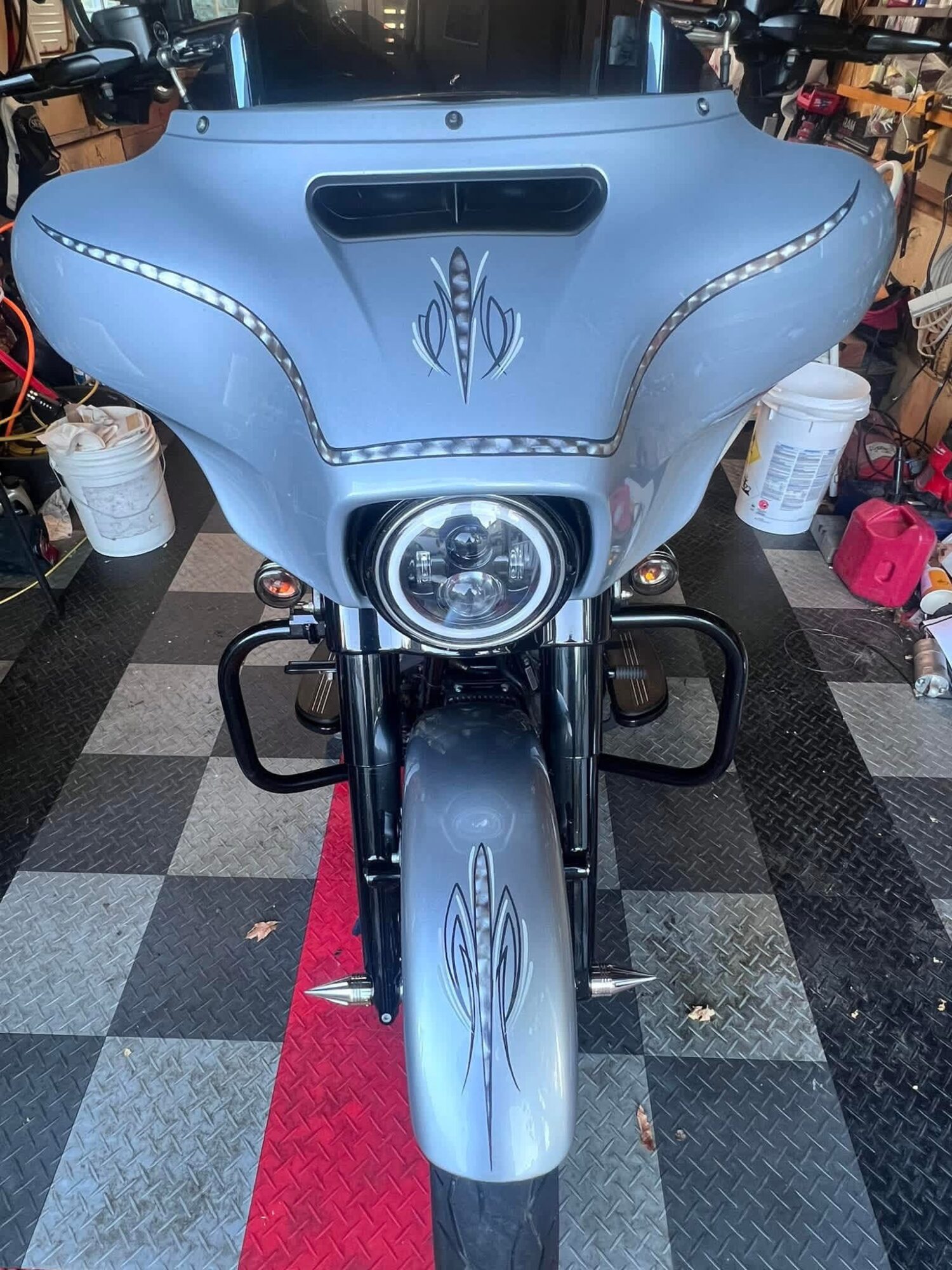 Front view of a motorcycle with a large front fairing, headlight, and decorative designs, parked indoors on a checkered floor.
