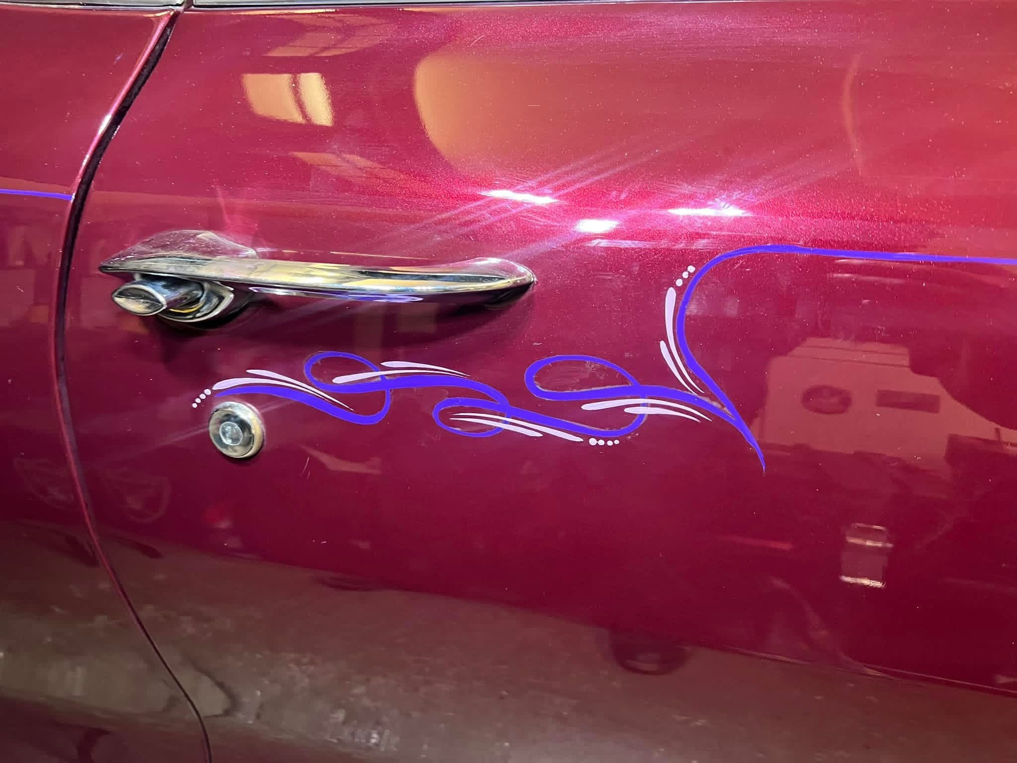 Close-up of a red car door with a chrome handle, blue flame decal, and a keyhole.
