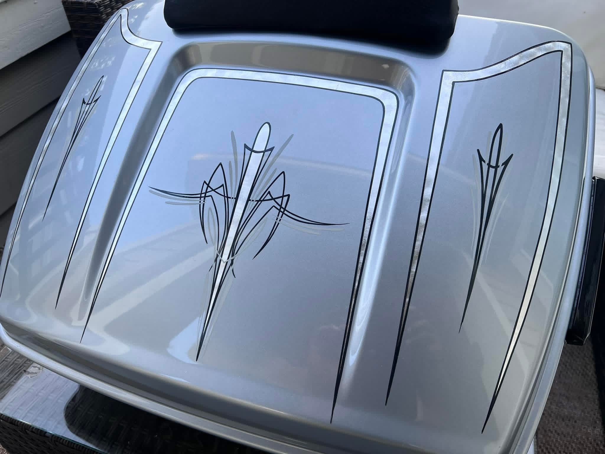 Car hood with decorative black pinstripe designs, reflecting the sky and surroundings, with a black object on top.