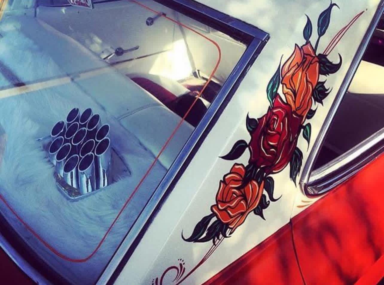 Close-up of a car with a floral tattoo design and a speaker on the rear window, showing part of the vehicle's side and rear.