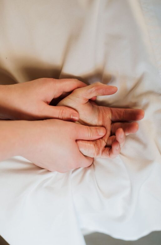 Two hands gently holding each other on a white fabric background.