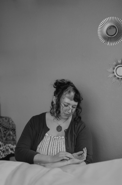 Woman with glasses sitting at a table, looking at her phone, with decorative wall art behind her.