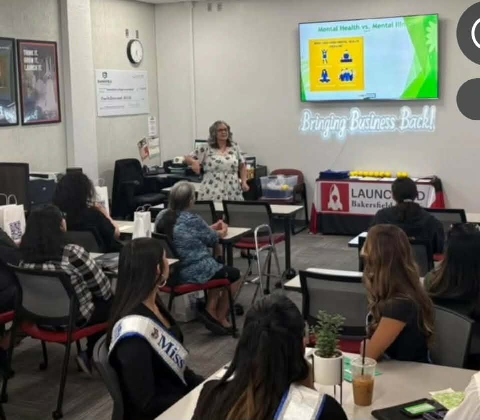 Woman presenting in a conference room with audience seated, screen displaying health information, and a banner on the table.