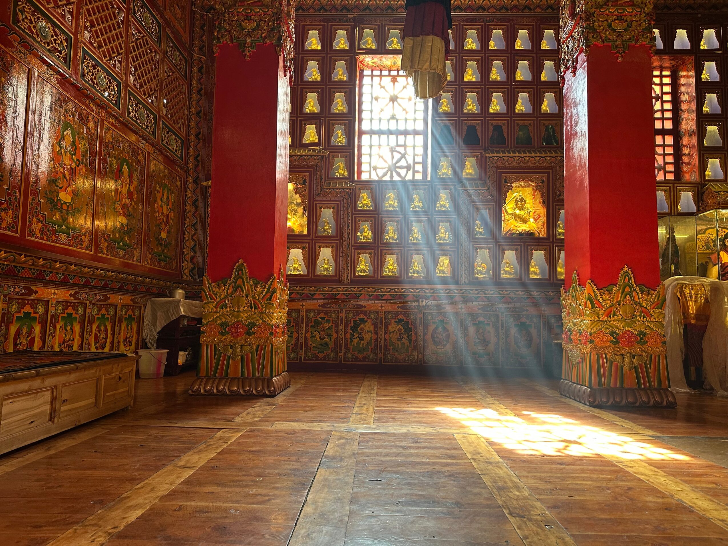 Sunlight streams through a window into a richly decorated room with red columns and ornate wall art.