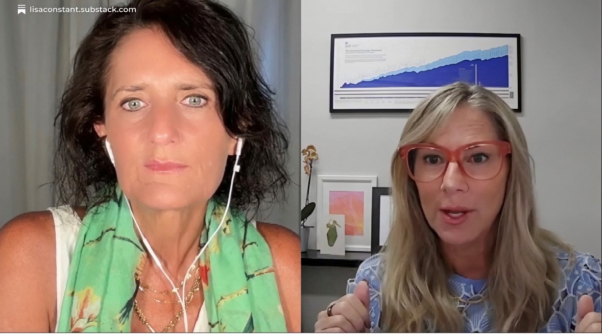 Two women engaged in conversation, one with dark hair and green scarf, the other with blonde hair and glasses, in an office setting.