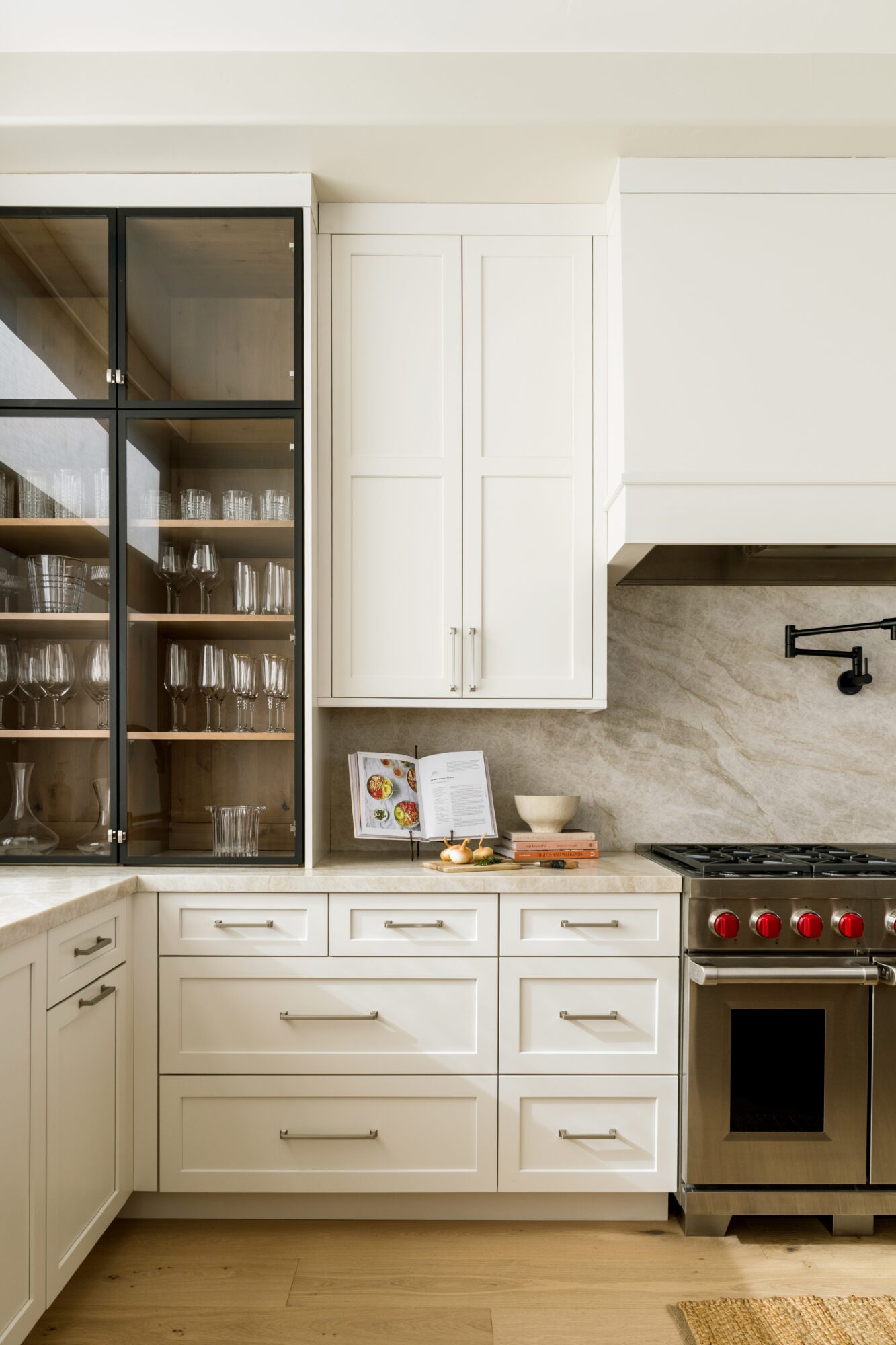 Kitchen with white cabinets, a glass-fronted cabinet, and a stainless steel stove with red knobs, on a wooden floor.
