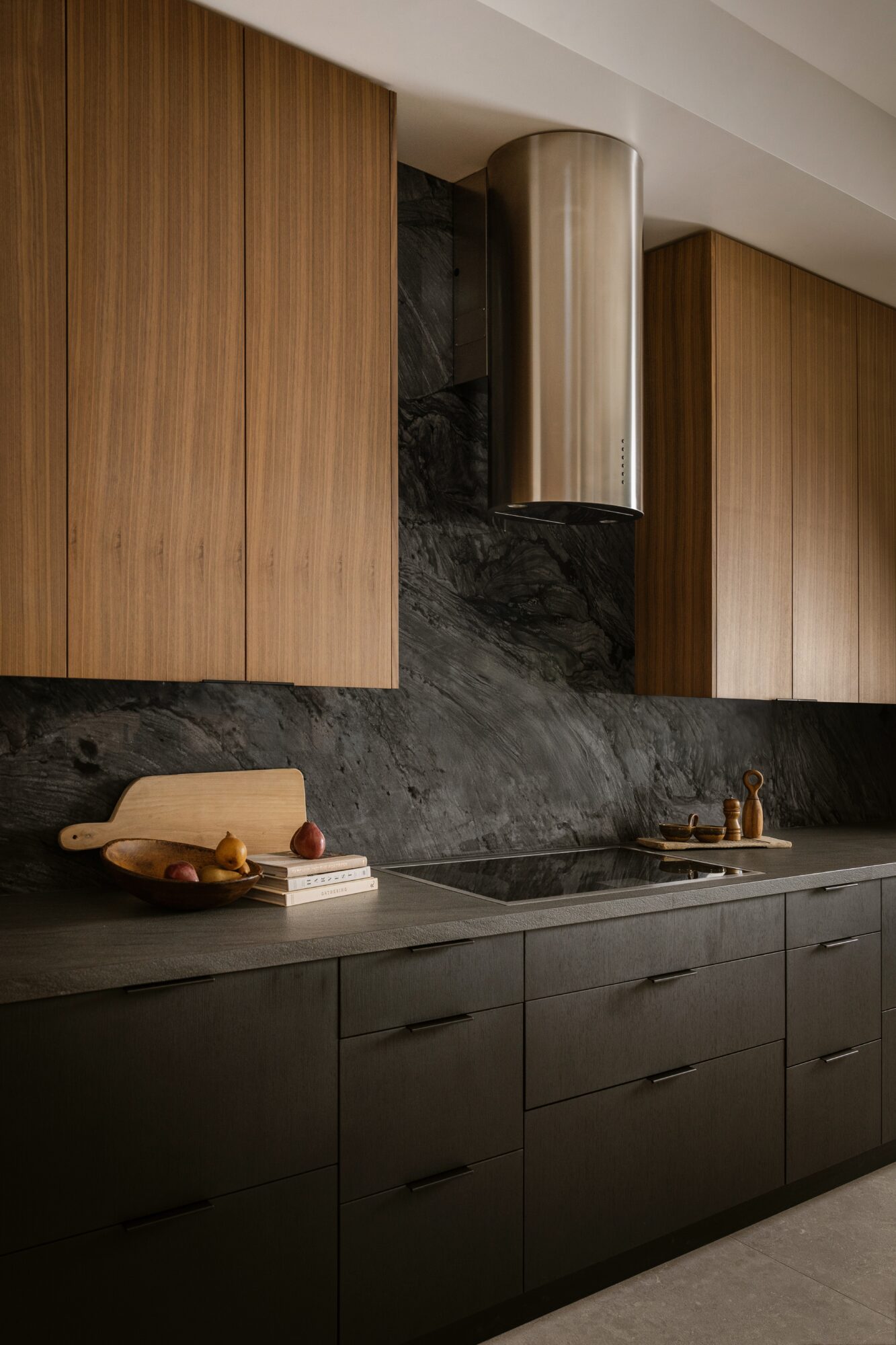Modern kitchen with black lower cabinets, wooden upper cabinets, a black marble backsplash, and a stainless steel range hood.