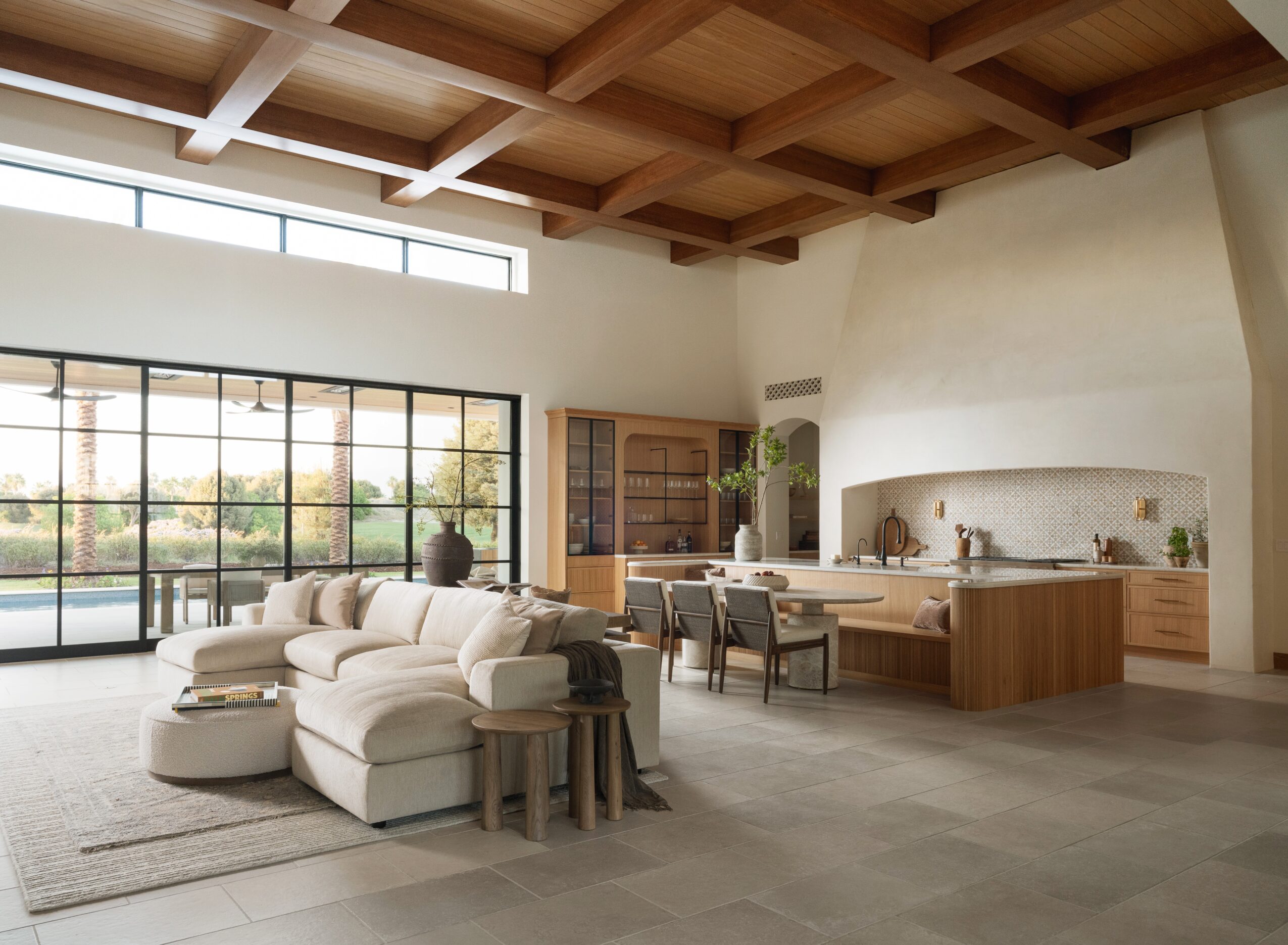 Open living and dining area with large windows, white sofa, wooden ceiling, and modern kitchen with island.