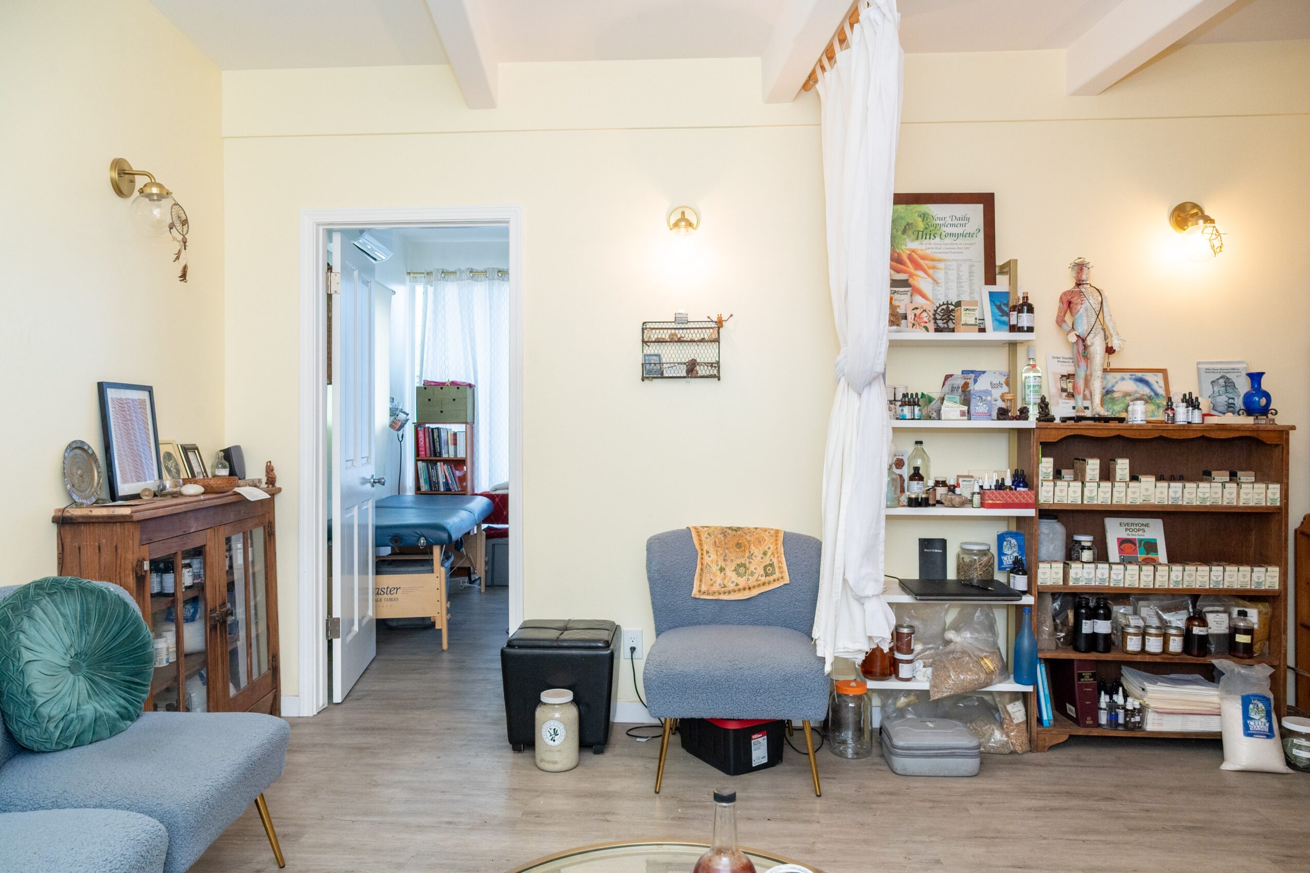 Living room with a blue armchair, bookshelf, and doorway to a bedroom, decorated with framed pictures and small decorative items.