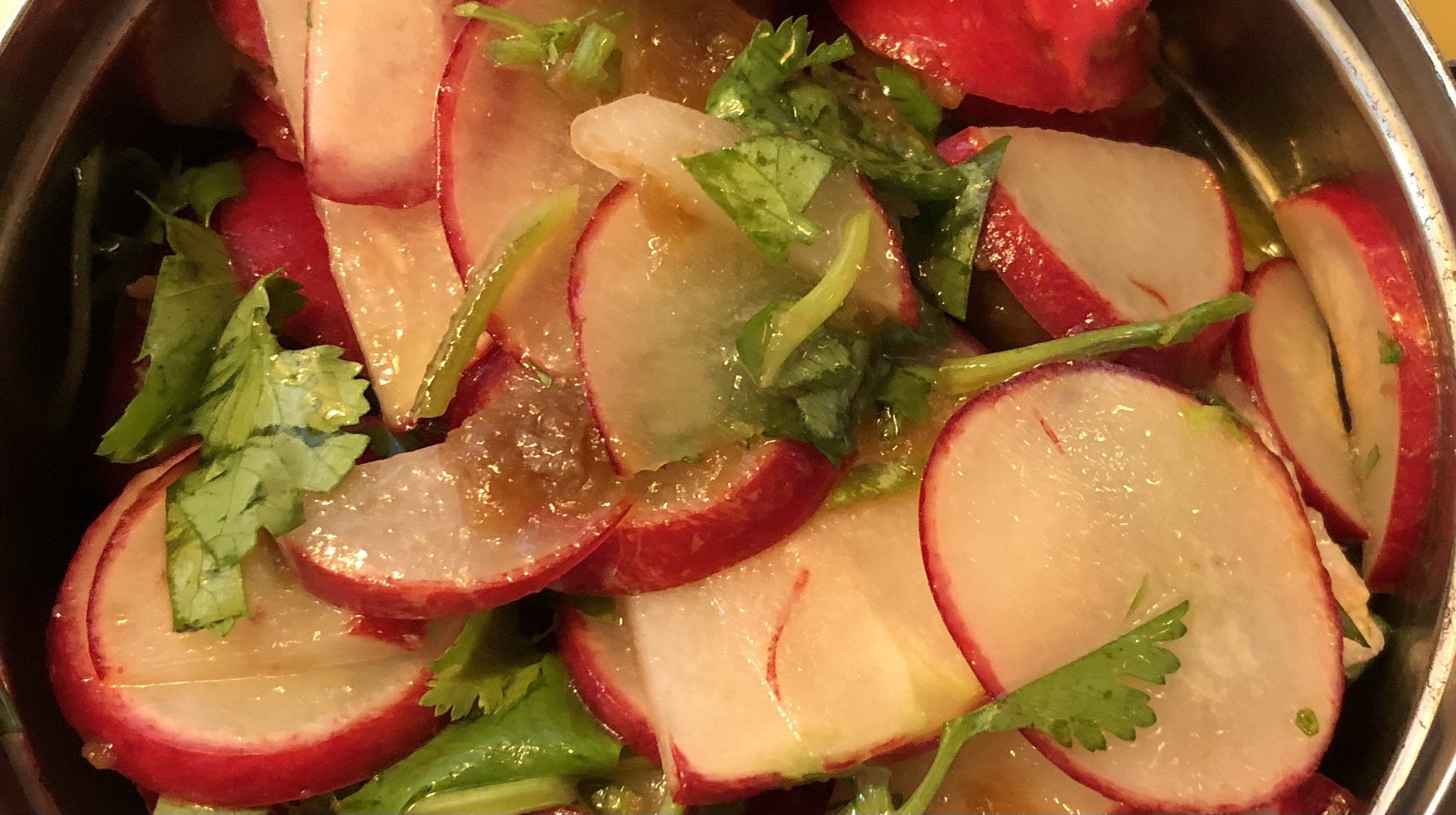 Sliced radishes, cucumbers, and cilantro in a bowl, fresh and colorful, with visible textures and vibrant colors.