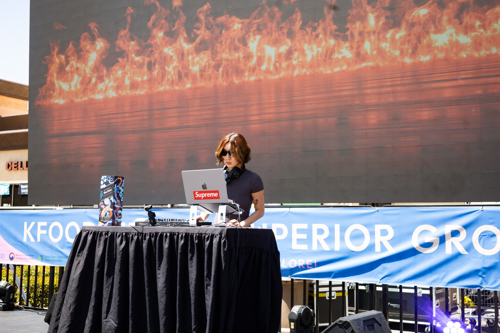 Person sitting at a table with a laptop and water bottle, with a large screen displaying flames behind them.