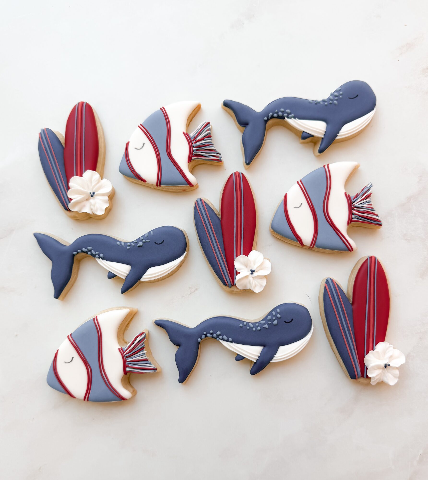 Decorative cookies shaped like whales, fish, and shells with red, blue, and white colors, on a white surface.