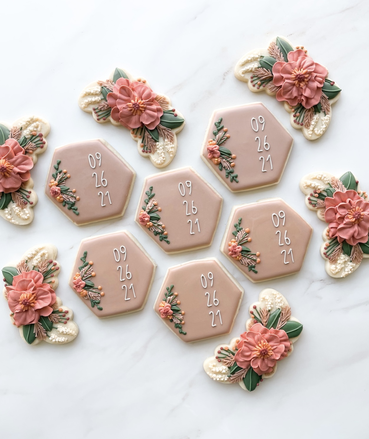 Decorative cookies with pink flowers and green leaves, some with date inscriptions, arranged on a white surface.