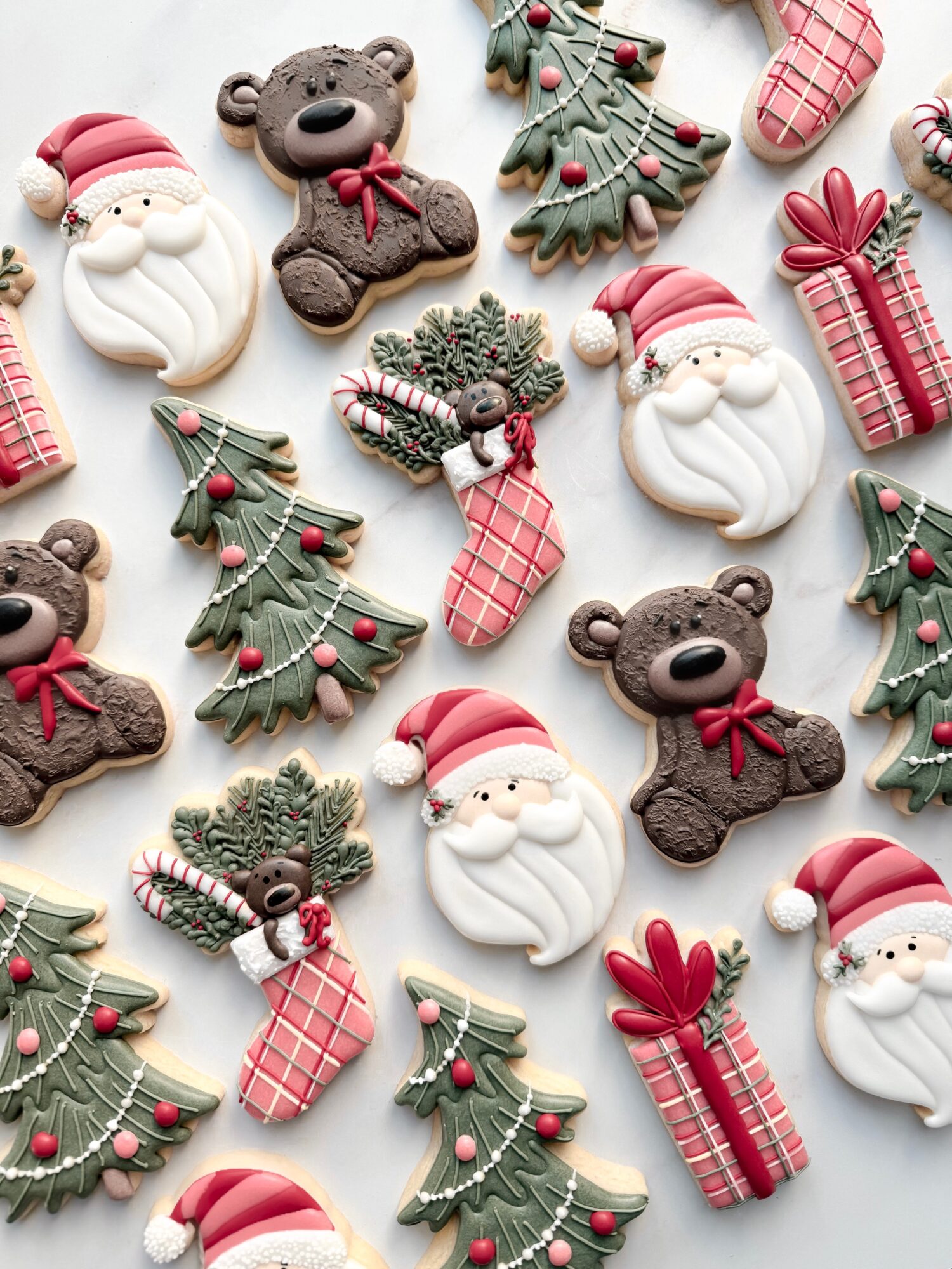 Christmas cookies shaped as Santa, bears, Christmas trees, stockings, and presents, decorated with icing and festive colors, arranged on a white background.