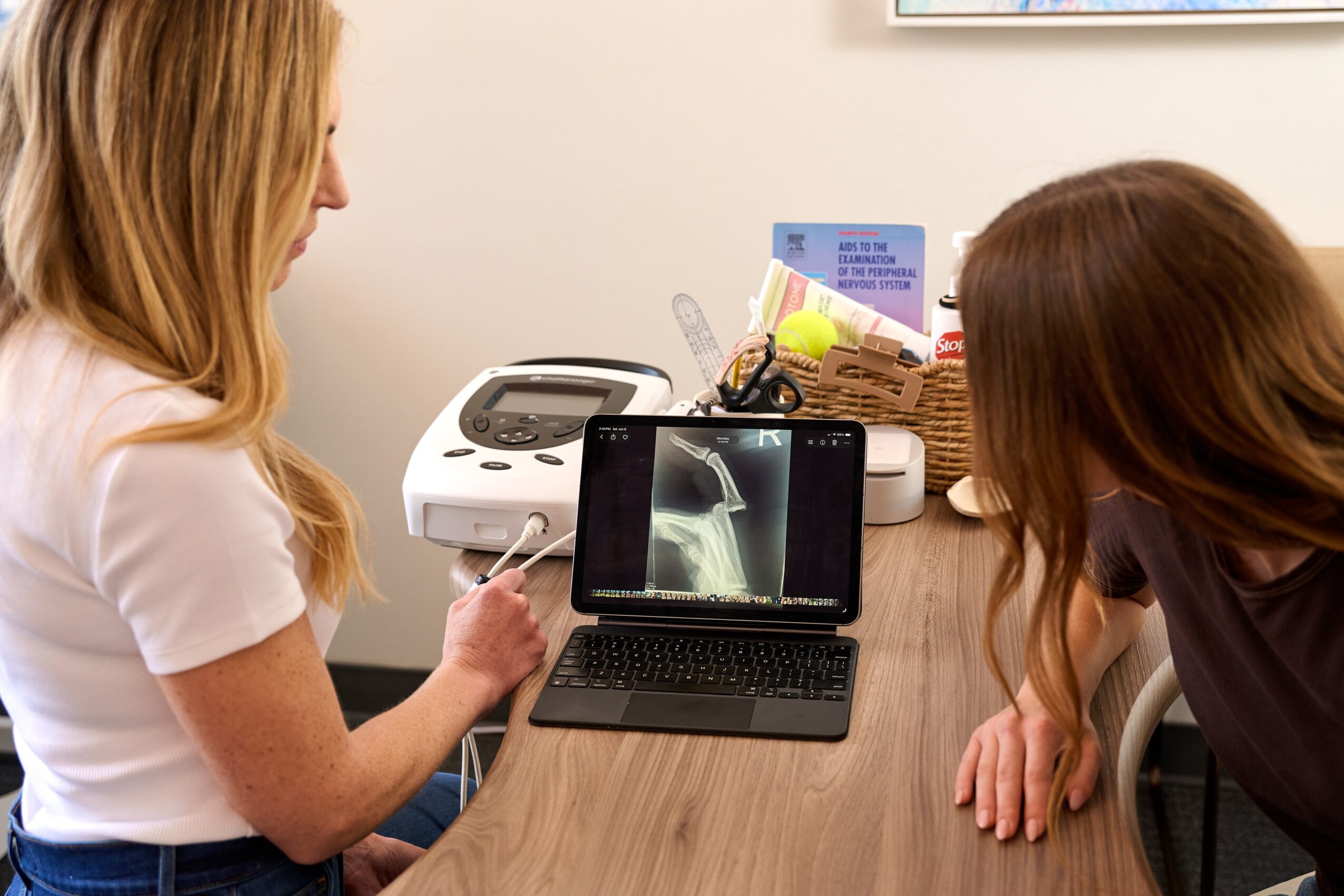 Two women look at an ultrasound image on a laptop screen on a wooden table.
