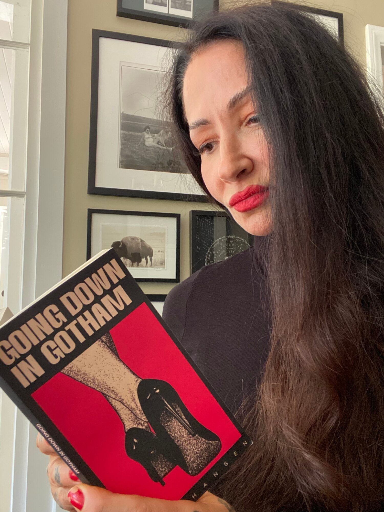 Woman with long dark hair and red lipstick looking at a book titled 'Going Down in Gothland' with a red and black cover.