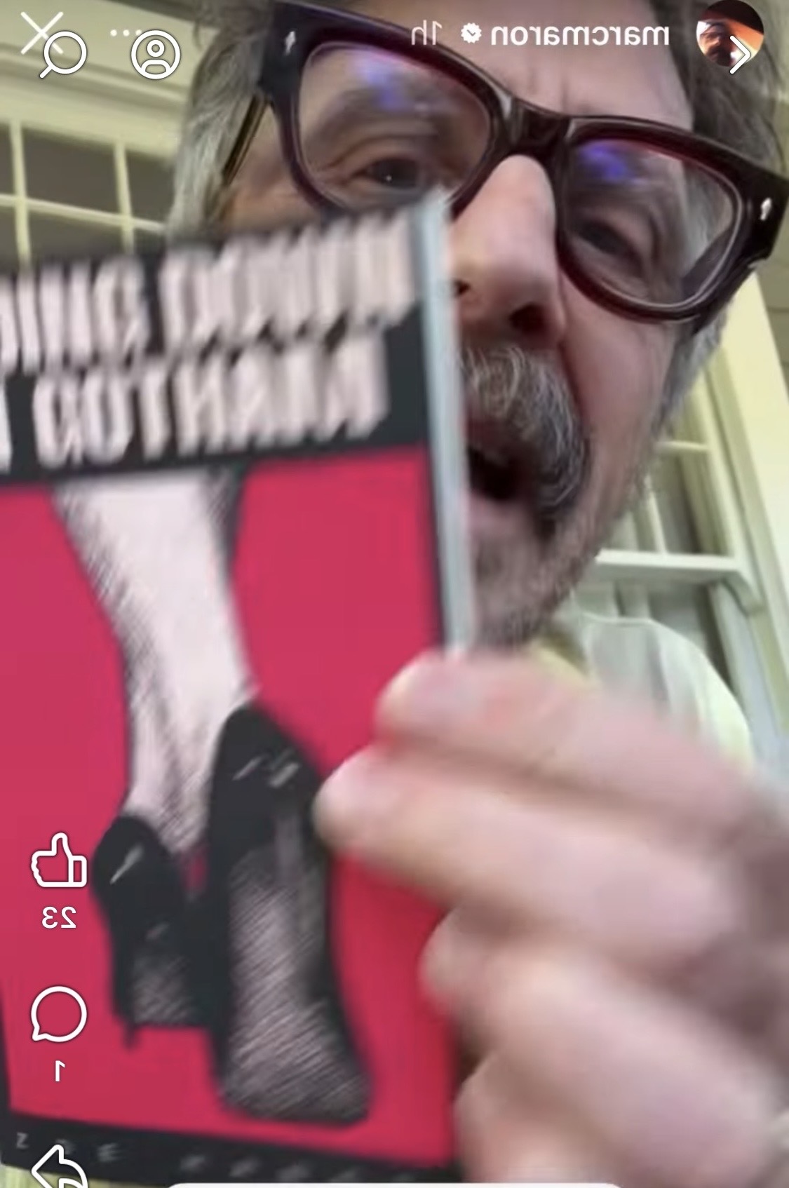 Person holding a book with a pink cover and black and white illustration, wearing glasses, close-up shot.