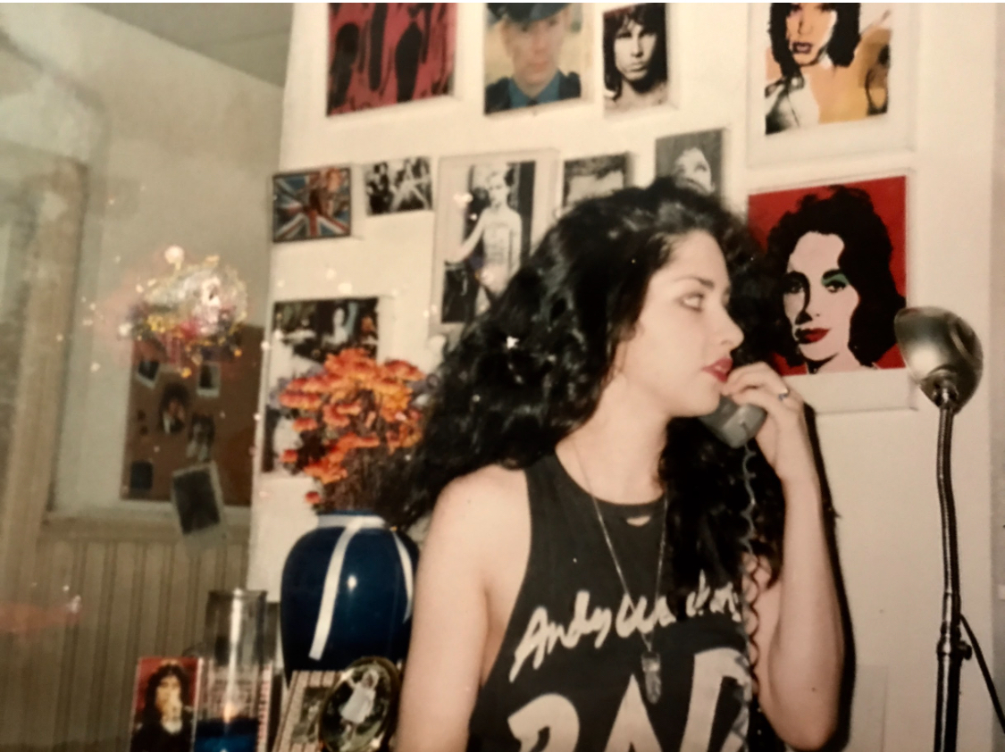 Side profile of a woman with dark curly hair in a room with photos and artwork on the wall.
