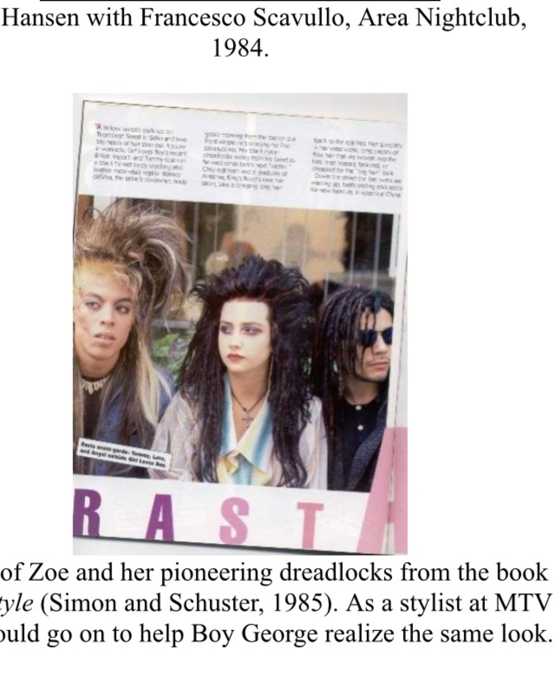 Photograph of three people with styled hair, holding a sign with partially visible text, in front of a building.