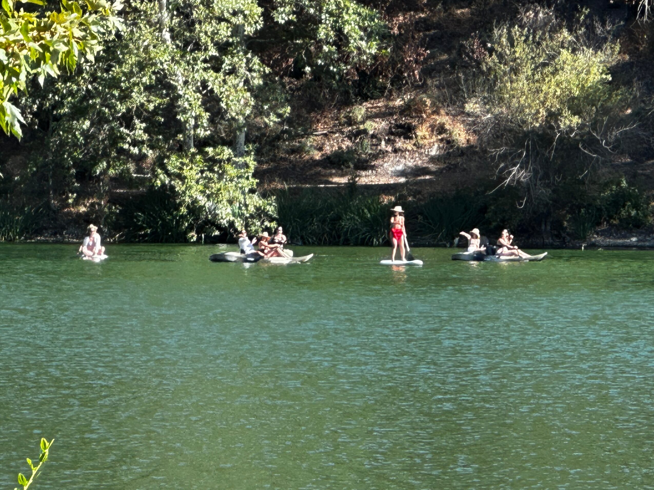 People paddleboarding and kayaking on a calm lake with trees and a rocky shoreline in the background.