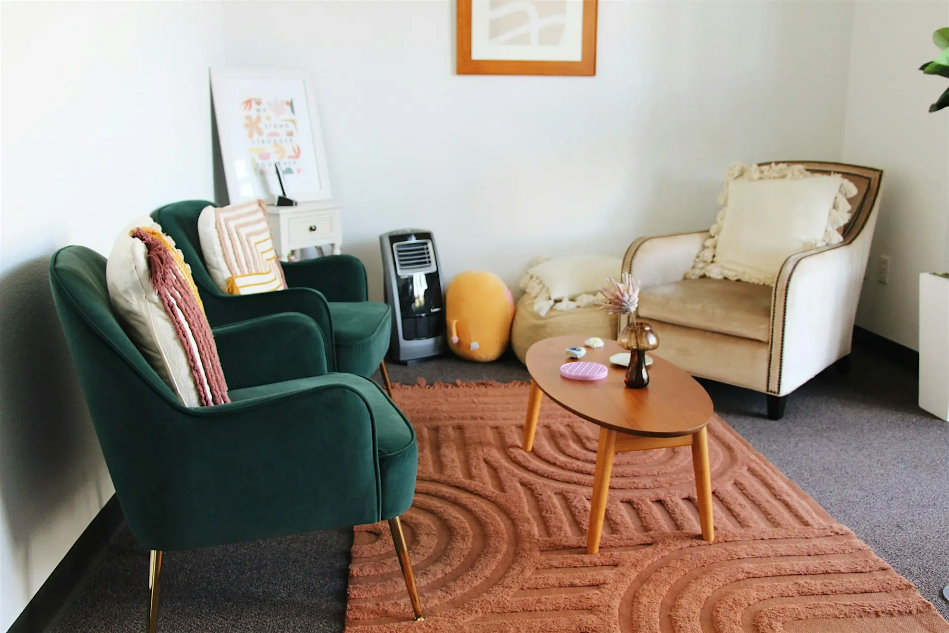 Living room with green and beige armchairs, a wooden coffee table, and a textured rug, with a white wall and framed artwork.