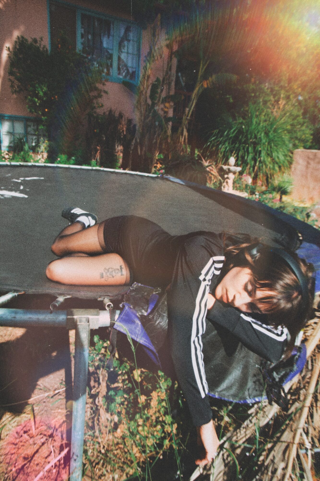 Person lying on a table outdoors, surrounded by trees and sunlight, wearing a black outfit with white stripes.