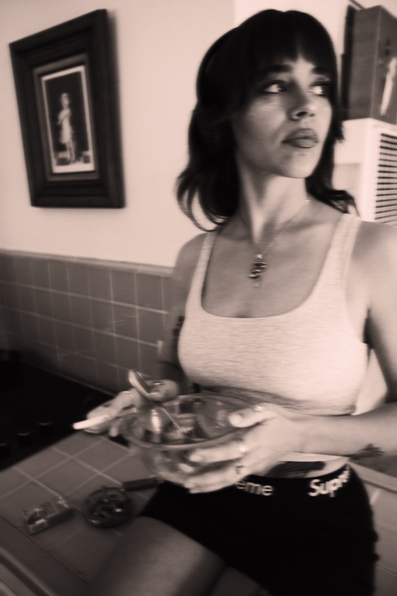Woman with dark hair and bangs holding a tray, standing in a room with framed picture on wall.